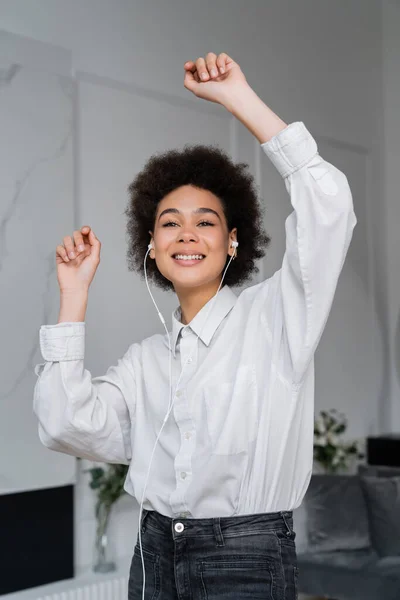 陽気なアフリカ系アメリカ人女性が有線のイヤホンで音楽を聴き家で踊り — ストック写真