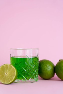 Pembe arka planda taze limonların yanında bardakta yeşil alkol içeceği
