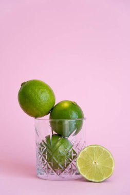 green fresh citrus fruit in faceted glass near half of lime on pink  clipart