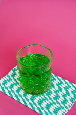 Yeşil alkol kadehinin yüksek açılı görüntüsü çizgili kağıt kamışların üzerinde pembe