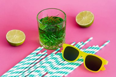 Güneş gözlüğü ve bir bardak yeşil alkol çizgili kağıt kamışların ve pembe limonların yanında içilir. 