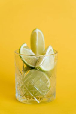 cool faceted glass with sliced fresh limes on yellow clipart