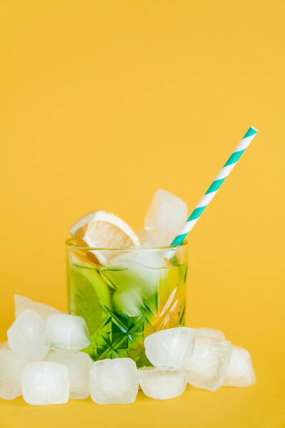 ice cubes and sliced lemons in glass with mojito drink on yellow 