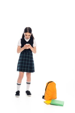Kitapların yanında akıllı telefon ve beyaz arka planda sırt çantası kullanan etekli bir kız öğrenci.