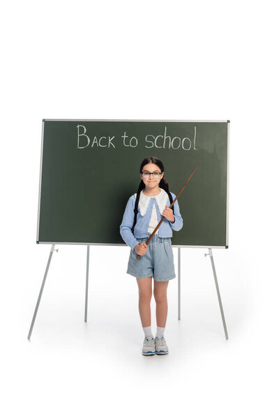 Full length of smiling schoolgirl holding pointer near chalkboard with back to school lettering on white background