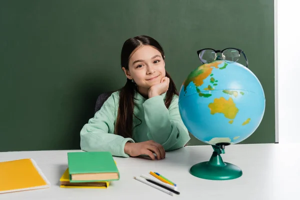 Lächelndes Schulkind Sitzt Neben Brille Auf Globus Und Kreidetafel Isoliert — Stockfoto