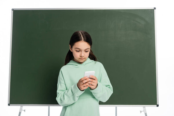 Preteen schoolkid using mobile phone near chalkboard isolated on white 