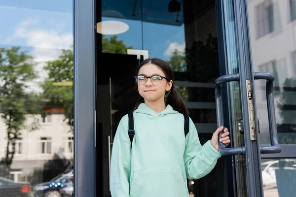 Pupil with backpack opening door of building outdoors