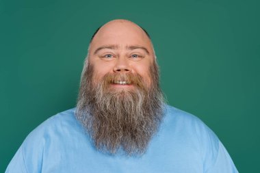 chubby and bald man with beard smiling at camera isolated on green
