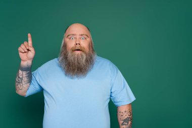 amazed overweight man with beard pointing up with finger isolated on green clipart
