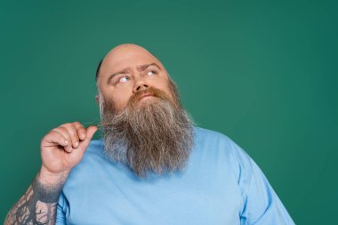 thoughtful man with overweight touching beard and looking away isolated on green