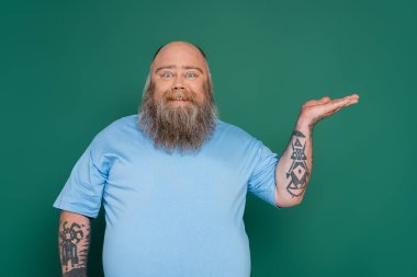 overweight man with beard smiling at camera and pointing with hand isolated on green