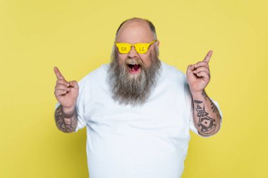 bold and bearded overweight man in glasses with sale lettering pointing with fingers isolated on yellow clipart