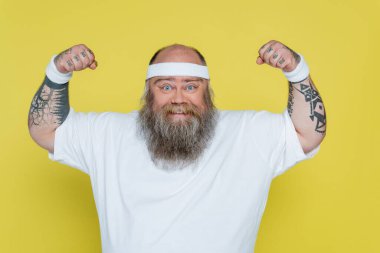 tattooed overweight sportsman demonstrating strength isolated on yellow
