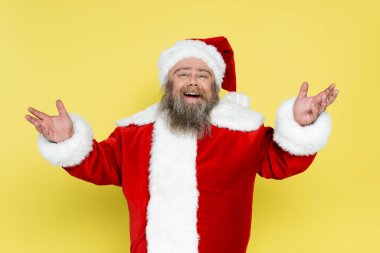 joyful and chubby santa claus showing greeting gesture isolated on yellow