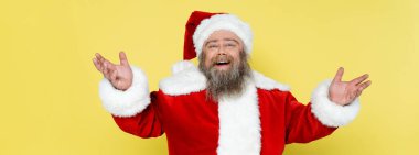 excited overweight santa claus showing greeting gesture isolated on yellow, banner
