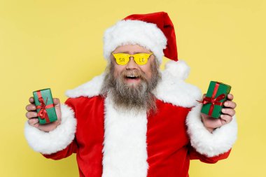 overweight santa claus in glasses with sale lettering holding presents isolated on yellow