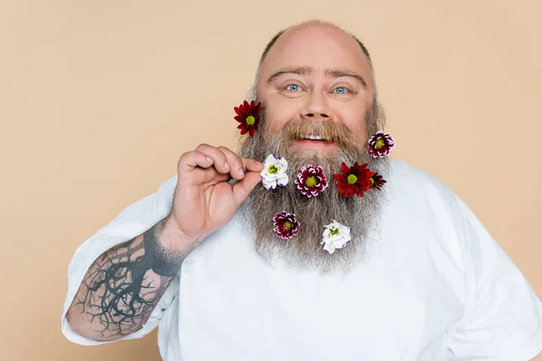 happy and chubby man showing beard with floral decor isolated on beige