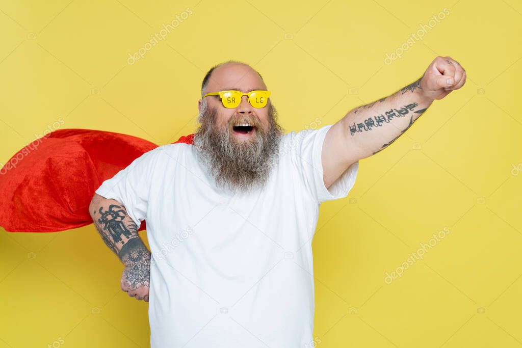 thrilled overweight man in superhero cape and glasses with sale lettering shouting isolated on yellow