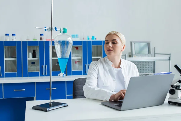 Cientista Usando Laptop Olhando Para Frasco Com Líquido Laboratório — Fotografia de Stock