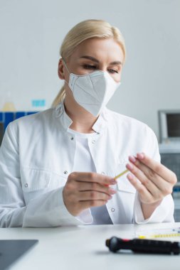 Koruyucu maskeli sarışın bilim adamı laboratuarda şırınga tutuyor. 