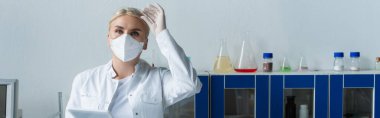 Scientist in protective mask holding goggles and digital tablet in lab, banner 