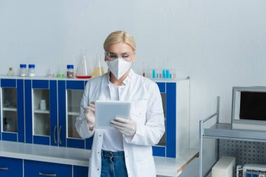 Laboratuvarda dijital tablet kullanan koruyucu maskeli bilim adamı 
