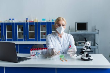 Koruyucu maskeli bilim adamı şişenin yanında şırıngalar ve laboratuarda test tüpleri tutuyor. 