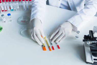 Laboratuvarda test tüpleri ve aşılar yanında şırınga tutan lateks eldivenli bilim adamı görüntüsü.