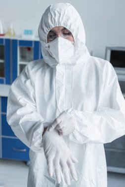 Scientist in hazmat suit and goggles wearing latex gloves in laboratory
