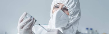 Koruyucu giysi ve maske giyen bilim adamı laboratuarda şırınga ve aşı tutuyor. 