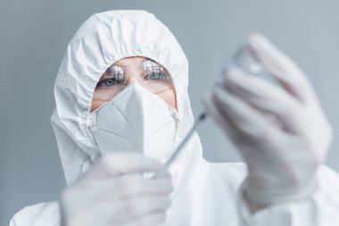 Tehlikeli madde giysisi ve gözlüklü bilim adamı laboratuarda bulanık şırınga ve aşı tutuyor. 