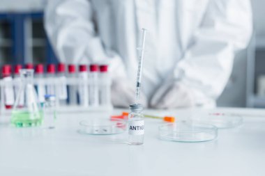 Bulanık petri kaplarının yakınındaki antijende şırınga ve laboratuvardaki bilim adamının kırpılmış görüntüsü. 
