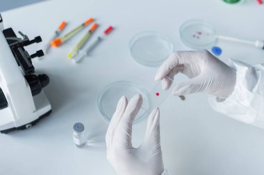 Laboratuvarda mikroskop ve petri kabının yanında cam tutan bilim adamı görüntüsü. 