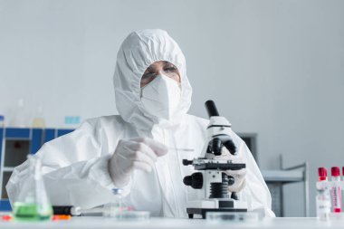 Laboratuvarda mikroskopla çalışırken koruyucu giysili bilim adamları cam tutuyorlar.