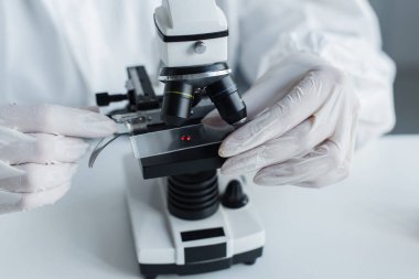 Cropped view of scientist in latex gloves using microscope in lab 