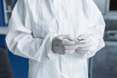 Cropped view of scientist in protective suit and latex gloves using mobile phone in lab 