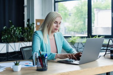 Psychologist using laptop near stationery in consultation room 