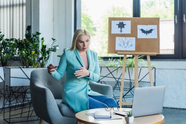 Psychologist gesturing while having video call on laptop in consultation room 