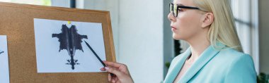 Side view of psychologist pointing at Rorschach test on board in consultation room, banner 