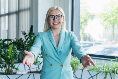 Cheerful psychologist outstretching hands at camera in consultation room 