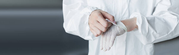 Cropped view of scientist in protective suit taking off latex glove in lab, banner 
