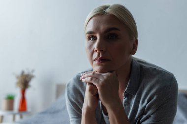 upset blonde woman with menopause looking away in bedroom 