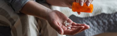 cropped view of woman with menopause holding bottle and pouring pills in hand, banner