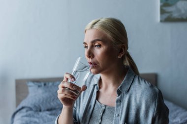 pensive woman with menopause drinking fresh water from glass 