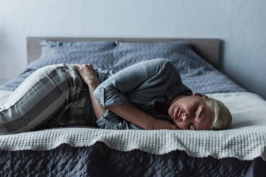 blonde woman lying on bed and suffering from stomach ache during menopause 