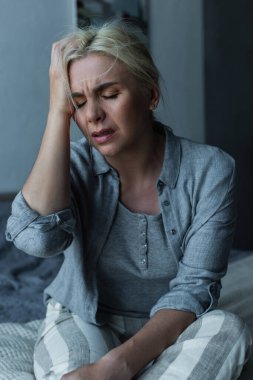 exhausted blonde woman touching head and having migraine during menopause 