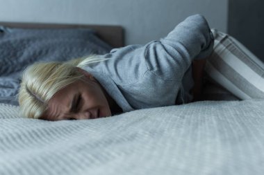 stressed woman lying on bed while feeling pain in stomach during menopause 