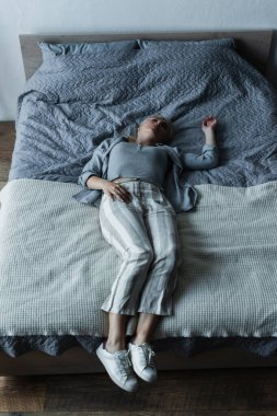 high angle view of blonde woman lying on bed while feeling pain in stomach during menopause 