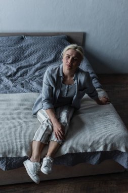 high angle view blonde woman sitting on bed while feeling pain in stomach during menopause 